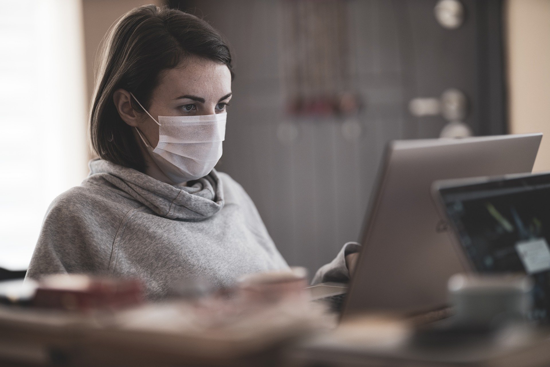 photo of young female student with face mask working on her laptop